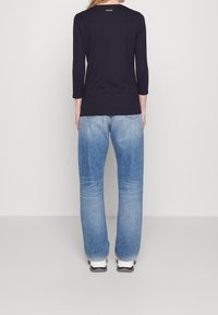 Marinblå långärmad tröja med rund hals, med en liten BOSS-logotyp på ryggen, i kombination med ljusblå vida jeans och vita sneakers.