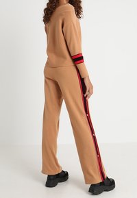 Beżowy dziany sweter i pasujące spodnie, z czarno-czerwonymi paskami po bokach. Luźny krój, teksturowana tkanina i swobodny design.