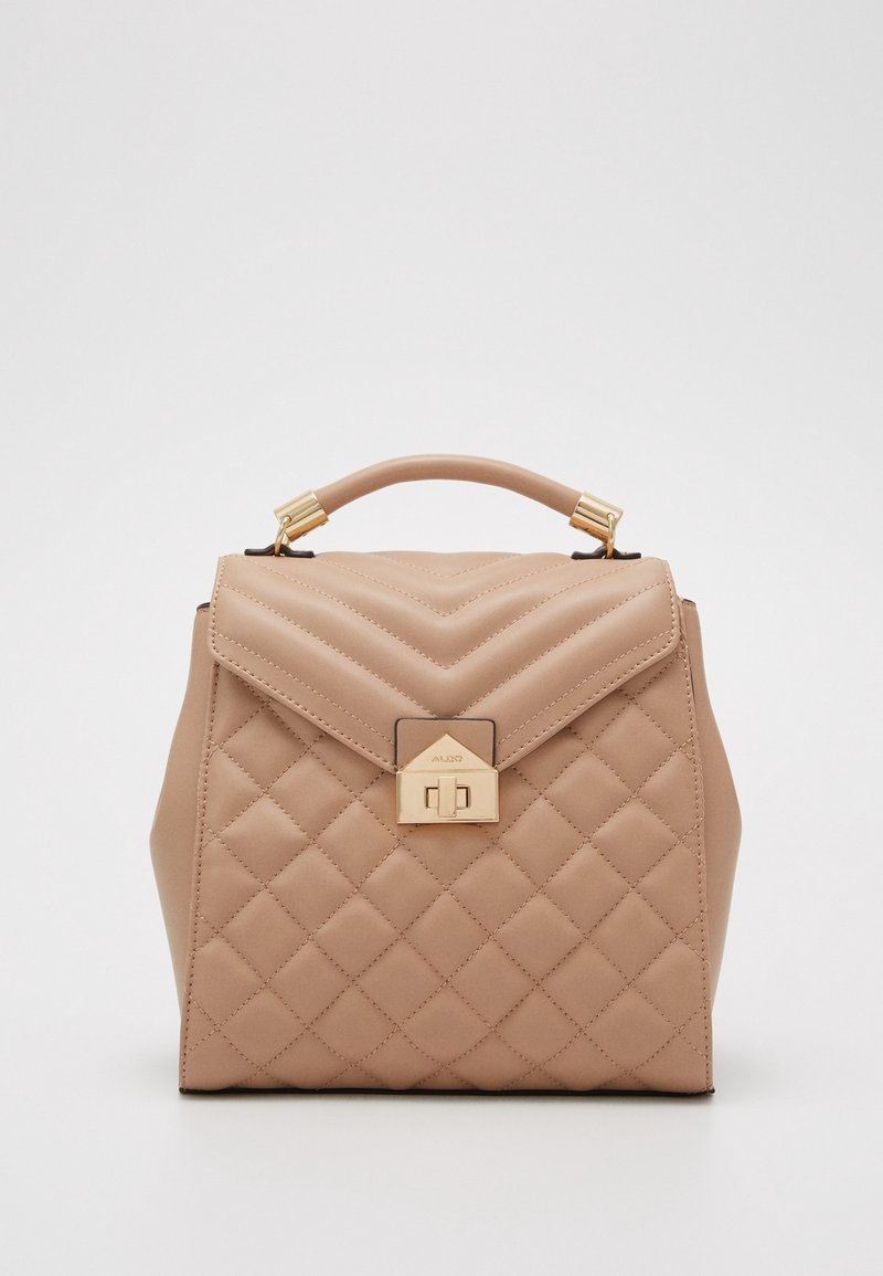 Sac à main matelassé beige avec poignée supérieure et fermeture à tour dorée sur un fond clair uni.