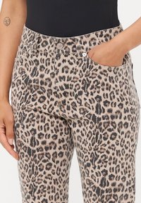 Vaqueros con estampado de leopardo en beige y negro, con un diseño estándar de cinco bolsillos, cierre de botón y un corte ajustado. Textura suave.
