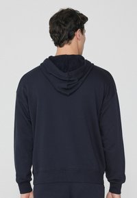 Marineblaue Kapuzenjacke aus weichem Stoff, mit einer Kordelzugkapuze, langen Ärmeln und einem gerippten Saum. Schlichtes Design, keine sichtbaren Logos.