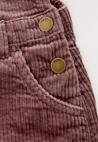 Velur z navpičnimi rebrci v vijolični barvi. Vključuje dve medeninasti gumbi z napisom "NEXT" blizu žepa. Mehka tekstura z natančnim šivom.