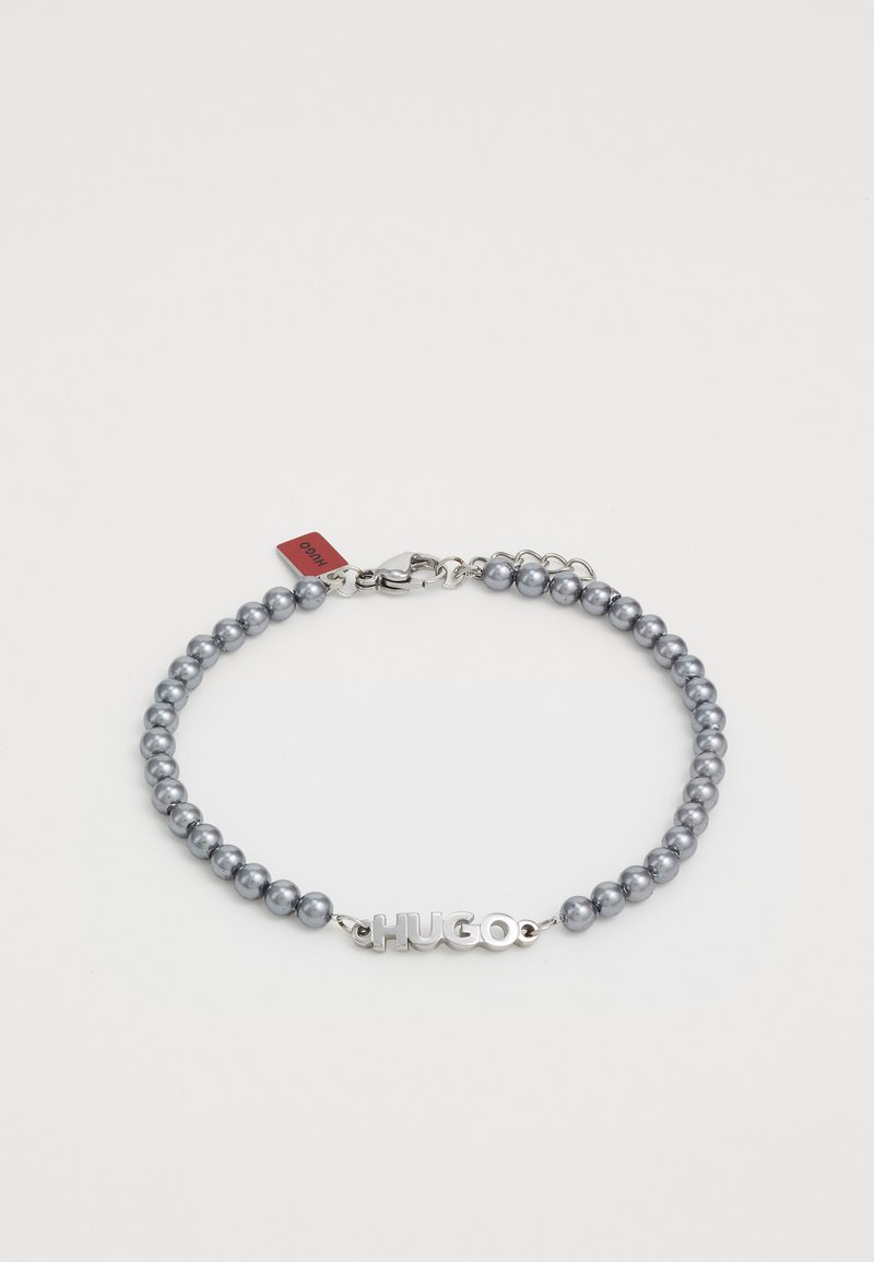 Grå pärlarmband med en metallklämma med "HUGO"-logotyp, med en silverfärgad kedja och en liten märkt tagg fäst.