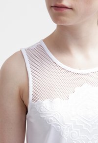 Top bianco senza maniche con un yoke in rete testurizzata e un motivo geometrico ricamato sul davanti, che mette in mostra elementi di design a strati.