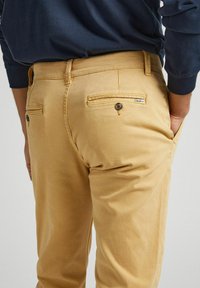 Pantalon kaki en coton, avec poches arrière à boutons et petite étiquette. Conception décontractée avec une coupe droite.