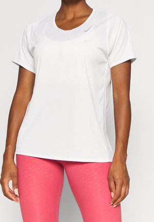 Femme portant un t-shirt blanc uni à manches courtes et des leggings rose vif avec un motif subtil, debout les bras détendus le long du corps.