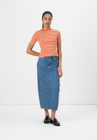 Stripet oransje og hvit kortermet skjorte kombinert med et langt blått denimskjørt; svarte loafers fullfører antrekket.