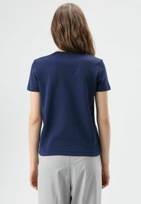 Marineblauw T-shirt met korte mouwen en een ronde hals, gemaakt van gladde stof, gecombineerd met lichtgrijze broek; strak, minimalistisch ontwerp.