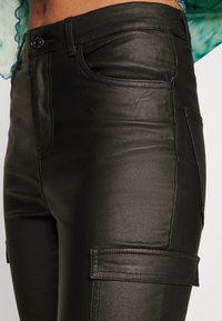 Czarne spodnie z sztucznej skóry o gładkiej fakturze, z tradycyjnymi kieszeniami oraz kieszenią cargo z boku dla zwiększenia funkcjonalności.