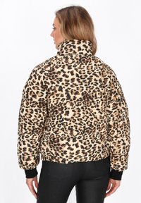 Pufjakke med leopardmønster og høj krave, beige baggrund, brune og sorte pletter, ribbede sorte manchetter og quiltet design.
