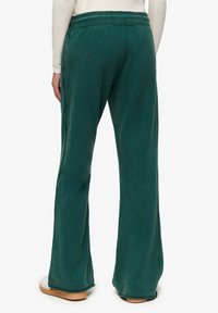 Grønne, udvidede sweatpants med en blød tekstur og et elastisk taljebånd. Stoffet har en let glans og glat finish. Ingen synlige lommer.