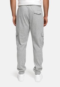 Gray sweatpants in soft fabric, featuring two side cargo pockets and one back pocket. Cuffed hems and paired with white sneakers.