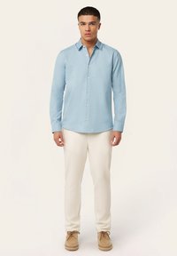 Lichtblauwe longsleeve shirt met een button-down kraag, textuurstof en witte knopen. Gepaarde met crèmekleurige broek en beige schoenen.