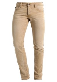 Jeans ajustados beige con una textura suave, que presentan cinco bolsillos, un cierre de cremallera y detalles de costura sutiles a lo largo de las piernas.