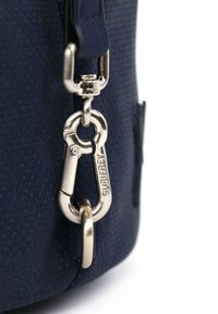 Tamsiai mėlynas perforuotas audinio maišelis su sidabro spalvos metaliniu sagtimi ir raktų pakabuku, turintis lygų paviršių ir suapvalintą formą.