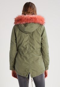 Olivgrüne Parka-Jacke mit einem rosa Kunstpelzkragen, Kordelzug in der Taille und einem etwas längeren Rückensaum. Strukturierter Stoff mit Metallknöpfen.