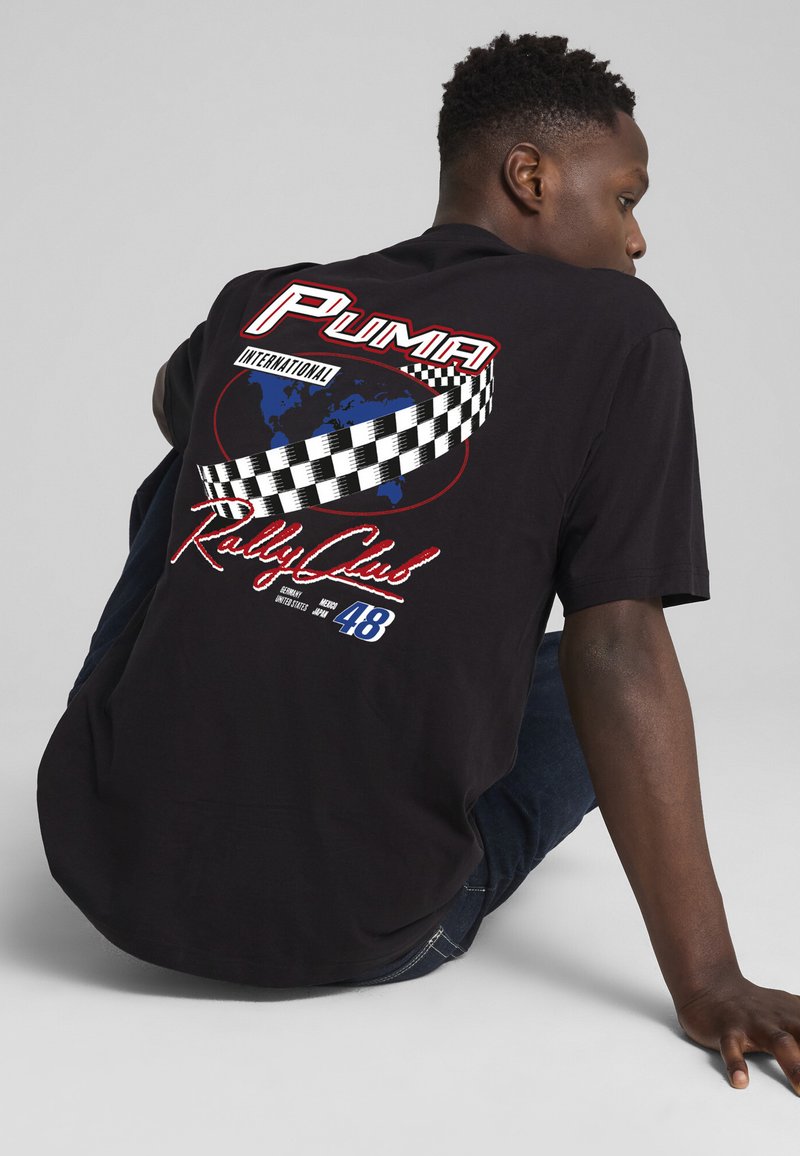Must musta T-särk mustast puuvillast, mille seljal on suur värviline graafika, millel on kaart, ruuduline muster ja tekst "PUMA International Rally Club 48."