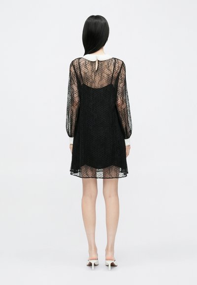 Svart blondekjole med lange ermer, hvit krage og detalj med nøkkelhull på ryggen. Gjennomsiktig stoff med teksturert polkagråmønster.