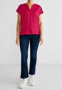 Top corto fucsia de manga corta con escote en V, combinado con jeans de campana azul oscuro y zapatillas blancas. Tejido suave, diseño minimalista.