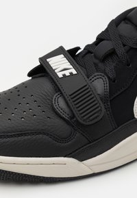 Černé kožen�é tenisky s texturovaným popruhem a logem "NIKE". Kulatá špička, perforované detaily a gumová podrážka s texturou.
