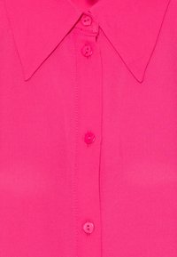 Fuchsia collared shirt made of smooth fabric featuring matching buttons down the front and neat stitching details.