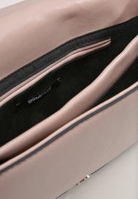 Borsa a tracolla in pelle sintetica rosa con texture liscia, dotata di fodera nera, tasche interne e un'etichetta con logo. Chiusura regolabile.