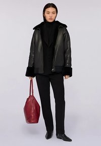 Svart läderjacka med pälskrage, kombinerad med svart polotröja, svarta byxor och en röd läderväska. Slim fit och minimalistisk design.