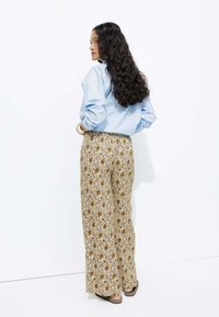 Chemise bleu clair associée à un pantalon large à motifs. Le pantalon présente une base beige avec des motifs floraux jaunes et noirs.