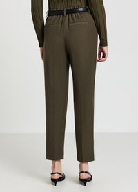 Vue arrière d'une personne portant un pantalon sur mesure olive, une ceinture noire, un pull côtelé et des sandales à talons noires, le tout sur fond blanc.