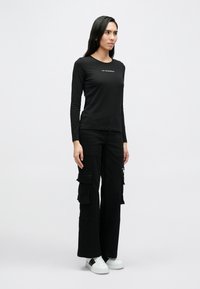 Svart langermet skjorte med rund hals, kombinert med svarte cargobukser med flere lommer og hvite joggesko.