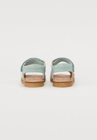 Baksidevisning av åpne sandaler med lyseblå lærremmer, en treinnersåle og en tan gummisåle med et minimalistisk design.