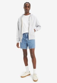 Hanorac zip-up gri deschis cu șnur, tricou alb, pantaloni scurți din denim albastru, șosete albe și adidași bej. Material neted și stil casual.