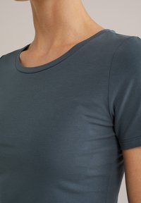 Tricou scurt, ajustat, cu mânecă scurtă, de culoare albastră închisă, realizat dintr-un material neted, cu decolteu rotund și design fără cusături la umeri.