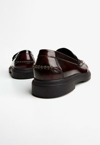 Dark brown leather shoes with a smooth finish, featuring a woven accent on the back, rounded shape, and black rubber soles.