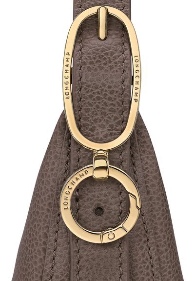 Graue Lederhandtasche mit einem goldfarbenen Hardware-Loop und Ring, auf dem das eingravierte "LONGCHAMP"-Logo zu sehen ist. Strukturierte Oberfläche mit genähten Akzenten.