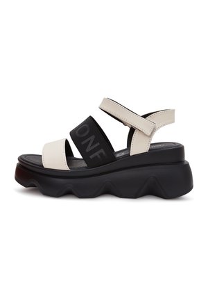Sandale plateforme noire épaisse avec des brides en cuir beige et une large sangle élastique noire sur le pied comportant un texte partiel "ONE".