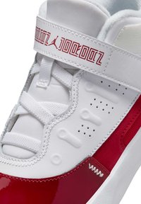 Baskets blanches et rouges avec une finition en cuir verni rouge lisse et brillant, des accents en mesh, et une sangle Velcro avec un logo à l'avant.
