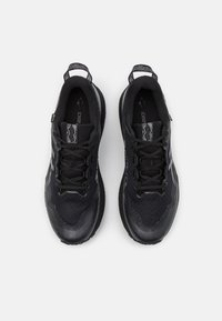 Baskets de sport noires en mesh et en matériau synthétique, avec une surface texturée, des lacets et des accents réfléchissants, dotées d'une semelle rembourrée.