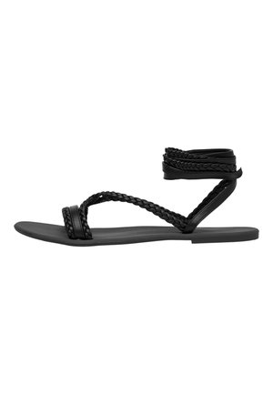 Sandali neri piatti con strappi intrecciati, caratterizzati da un design avvolgente per la caviglia. Realizzati in materiale sintetico con una texture liscia.