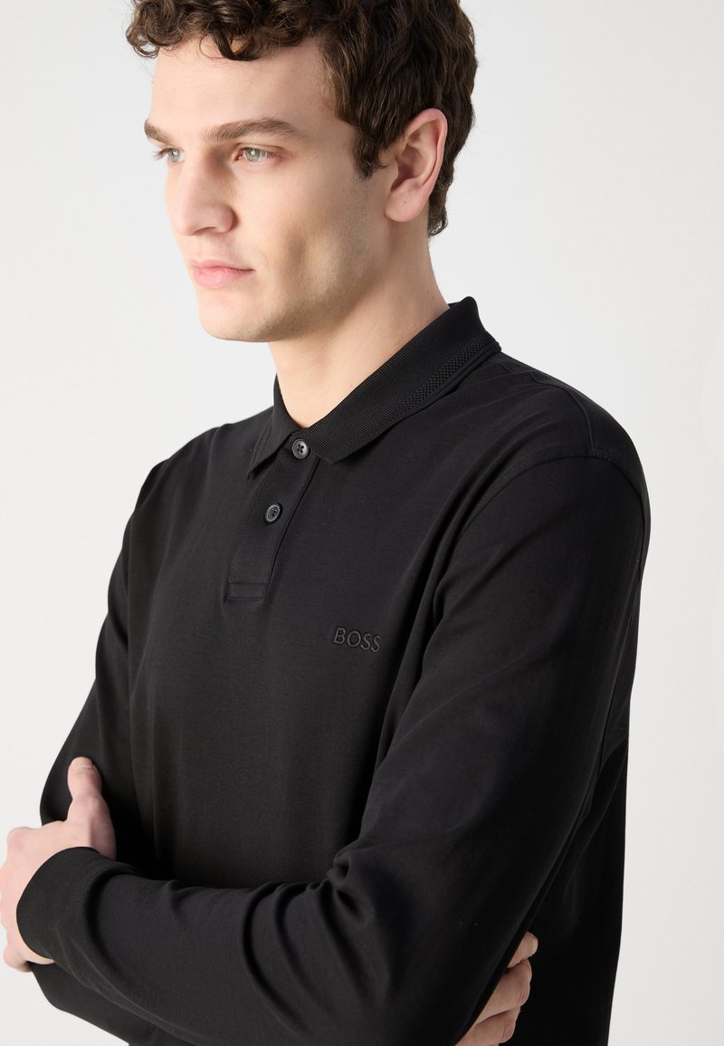 Schwarzes Langarm-Polohemd aus weichem Stoff. Mit einem Knopfkragen, dezentem Logo-Stick und lockerer Passform. Strukturiertem Halsausschnitt.