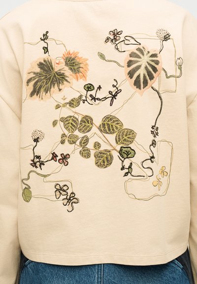 Μπεζ φούτερ με κεντητό βοτανικό σχέδιο που απεικονίζει διάφορα πράσινα και ροδακινί φύλλα, λουλούδια και κλήματα στην πλάτη.