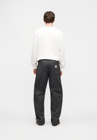 Γκρι παντελόνι εργασίας με φαρδιά εφαρμογή, με ετικέτα λογότυπου, δύο πίσω τσέπες και ανθεκτικό ύφασμα. Συνδυάζεται με λευκό πουκάμισο μακρυμάνικο.