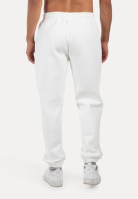 Bílé bavlněné tepláky s elastickým pasem a manžetami, vyznačující se hladkou texturou a volným střihem, doplněné o bílé tenisky.