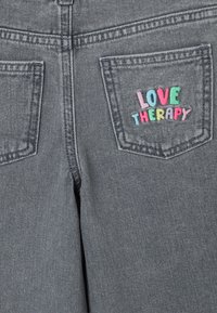 Jeans in denim grigio con la scritta ricamata "LOVE THERAPY" in rosa, blu e verde sulla tasca posteriore, con un classico design a cinque tasche.