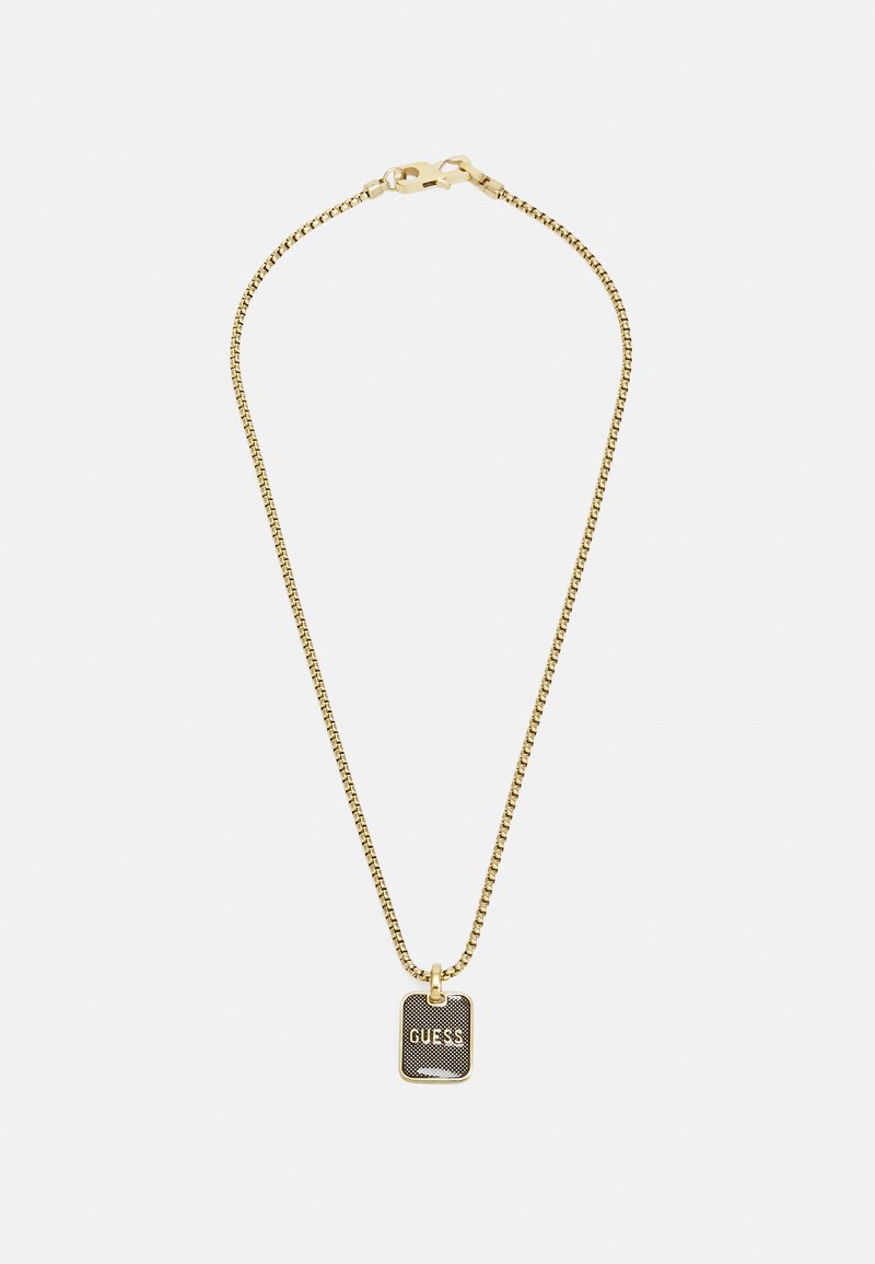 Gouden ketting met een rechthoekige zwarte hanger, met het woord "GUESS" in een vet lettertype. Gladde textuur, minimalistisch ontwerp.