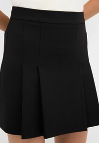 Jupe plissée noire avec une taille structurée, fabriquée dans un tissu lisse. Dotée d'une texture subtile et d'un design évasé.