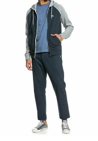 Navy zip-up hoodie with gray sleeves, paired with striped navy pants and gray sneakers. Lightweight material, casual fit, functional design.