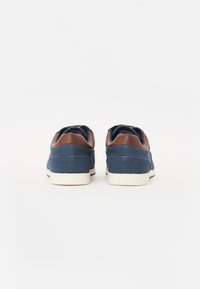 Dark blue canvas sneakers with brown leather accents, white rubber soles, and stitched detailing on heel and sides.