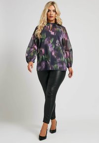 Genomskinlig blus med blommönster i lila och grönt, med en nyckelhålsringning och puffärmar, matchad med svarta skinnleggings.