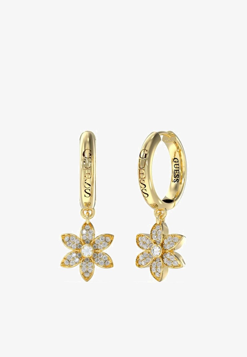 Orecchini a cerchio in oro con un design floreale, impreziositi da cristalli trasparenti. Il marchio "GUESS" è visibile sul cerchio.